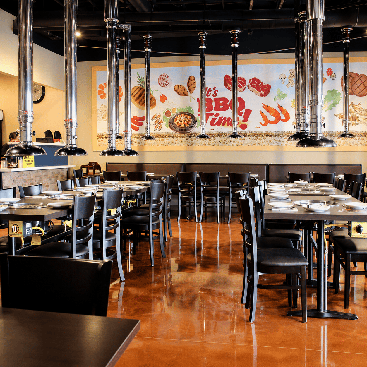 The KM.BBQ dining room: tables with built-in grills under chrome extraction ducts, with the painted mural along the back wall